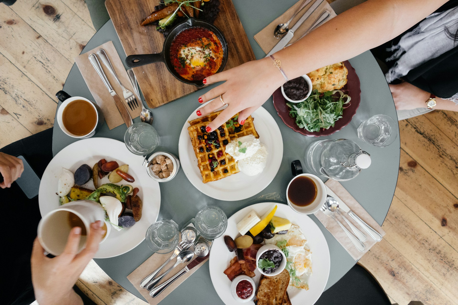 A table with food and hands reaching for it.