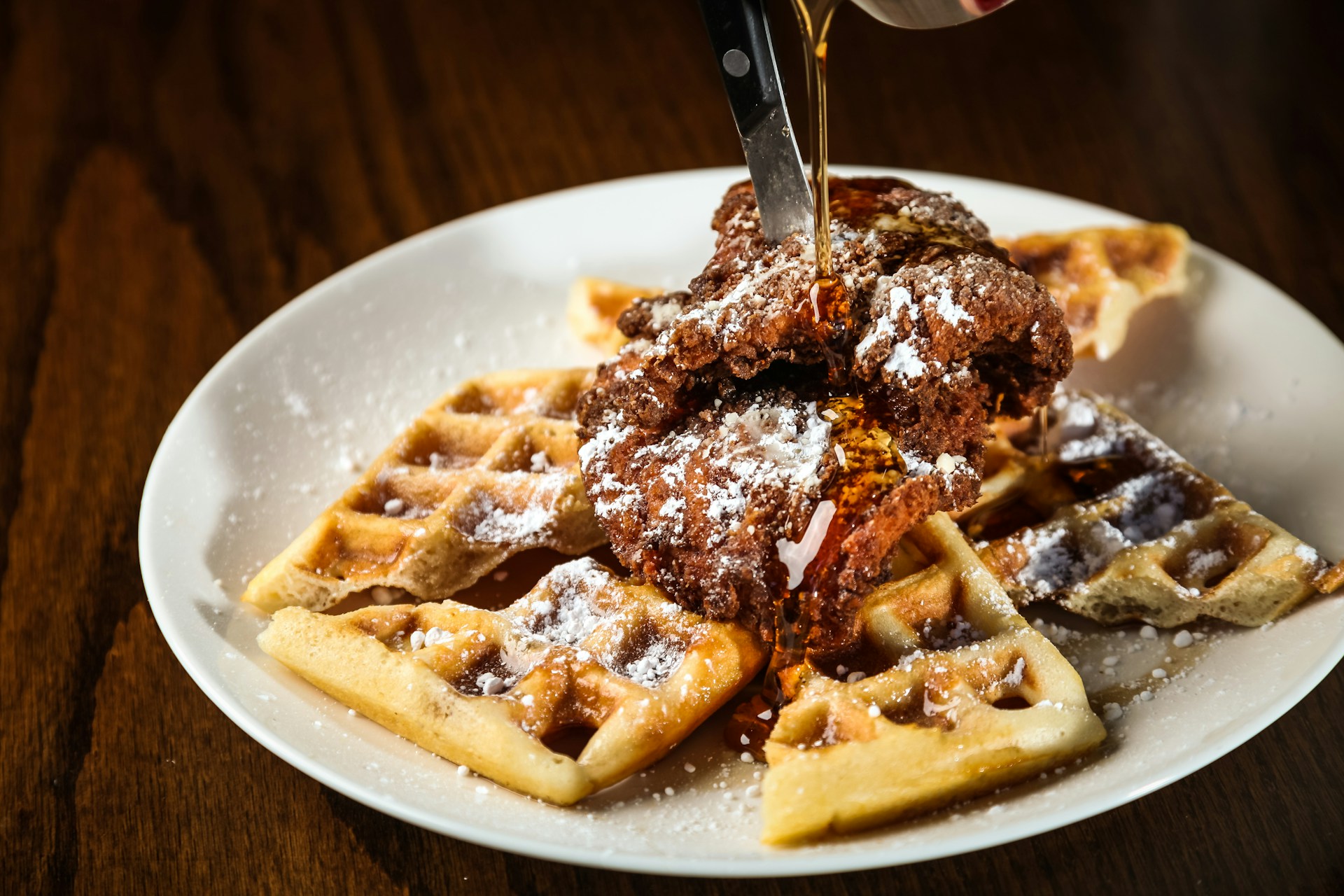 A plate of chicken and waffles being drizzled with syrup.