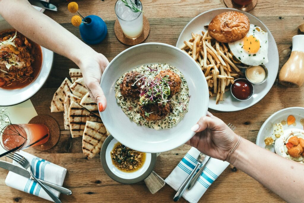 Overhead view of a table with food at a restaurant. An entree is being passed across the table.